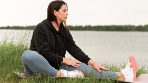 Serene outdoor yoga session by a lake with a woman stretching on a mat.
